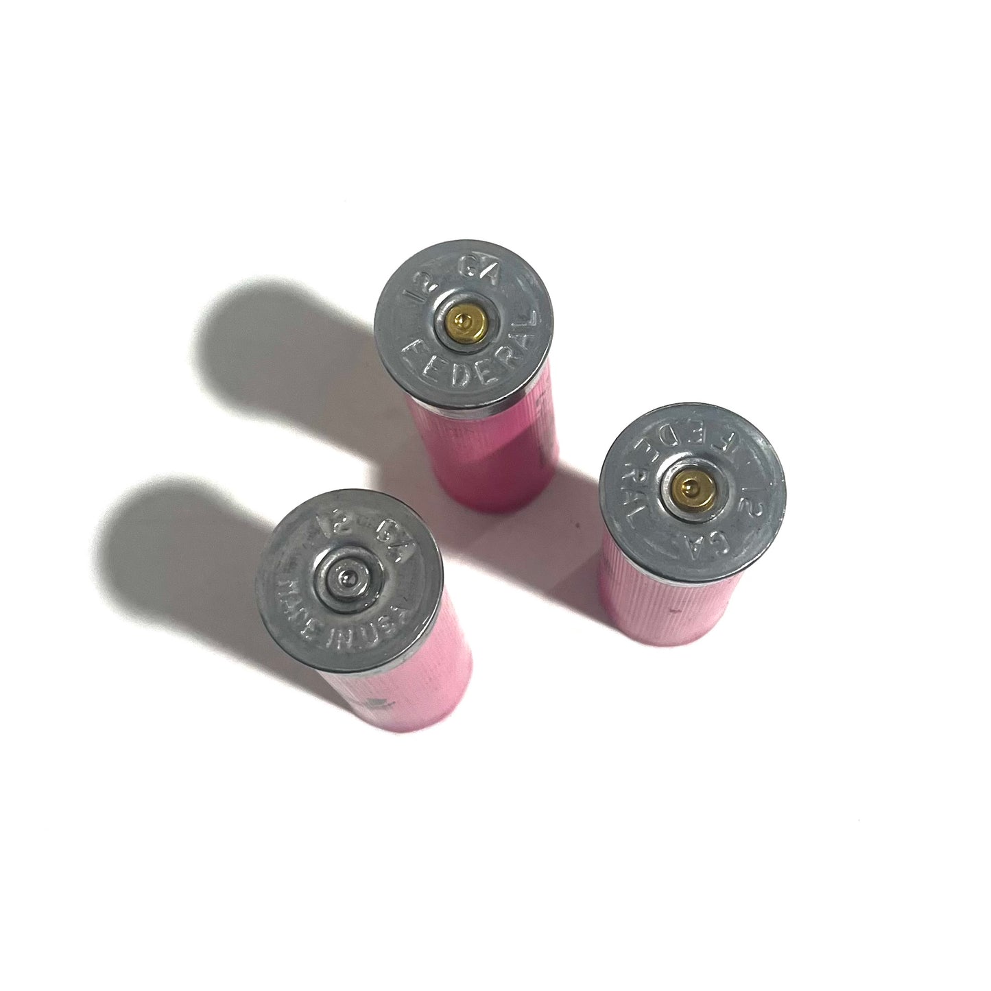 Silver brass bottoms of three pink Federal shotgun shells showing 12 GA headstamps