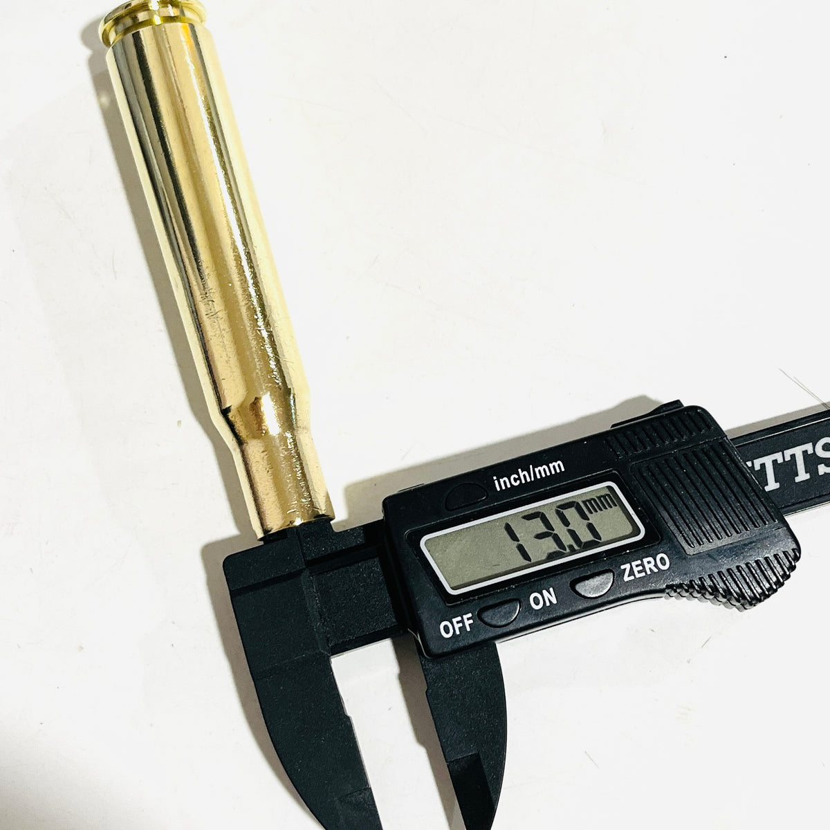 Digital caliper measuring the case mouth of a hand-polished .50 BMG brass spent casing at 13.0 mm on a white background