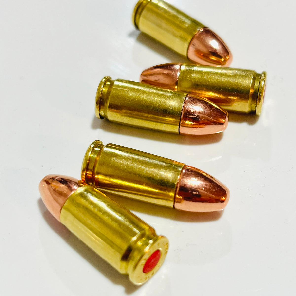 Five spent brass dummy rounds with copper round-nose bullets lying staggered in alternating directions on white