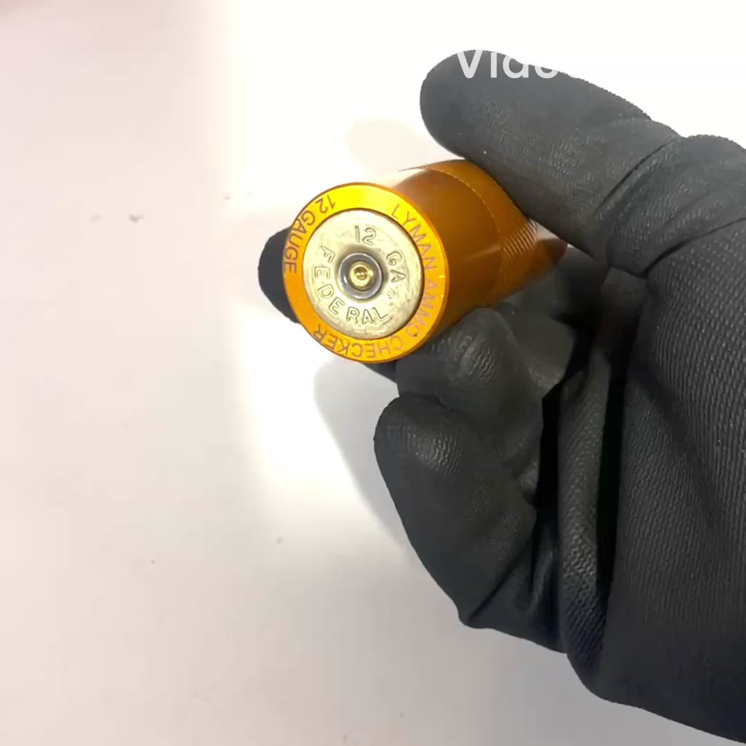 Hand in a black latex glove using a shotgun shell sizing tool to confirm a 12 gauge dummy round has been properly sized