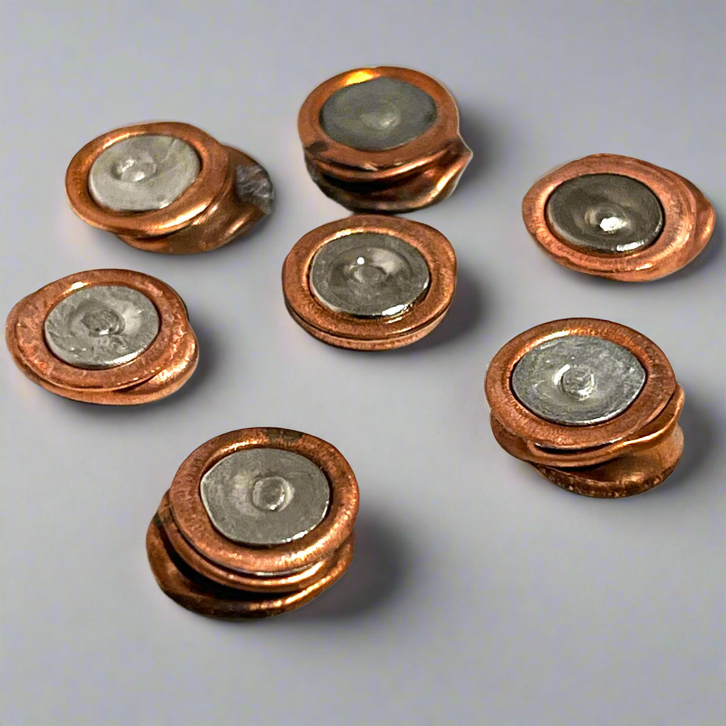 Seven copper and silver two-tone primer studs scattered on a smooth grey background.