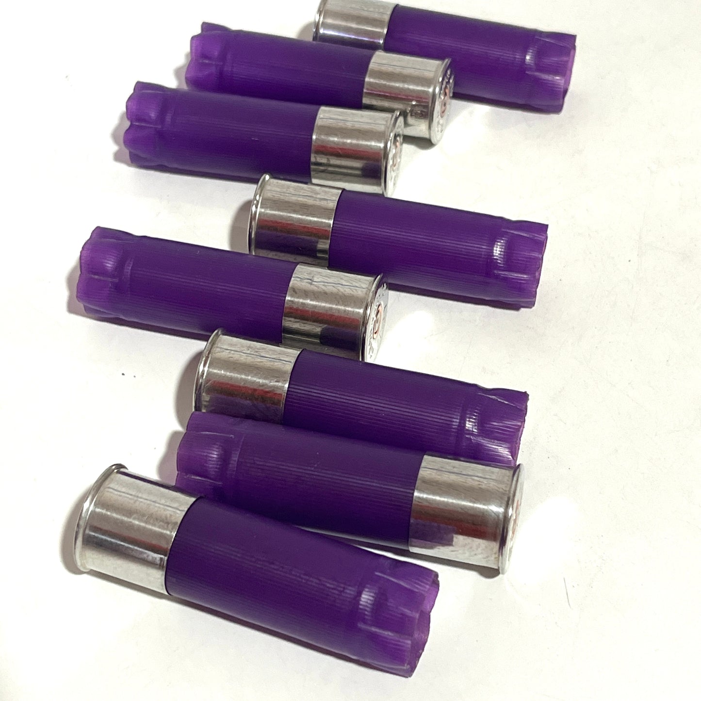 7 purple 12 gauge shotgun shell hulls with silver bases, lying in rows on a white background