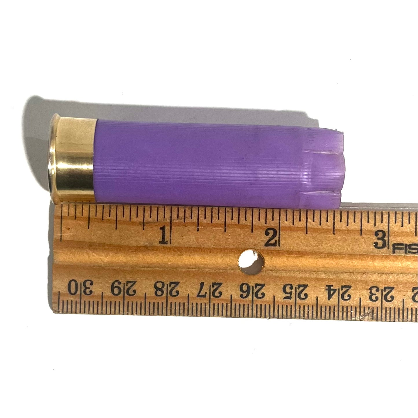 Purple 16 gauge shotgun shell hull next to a wooden ruler for scale