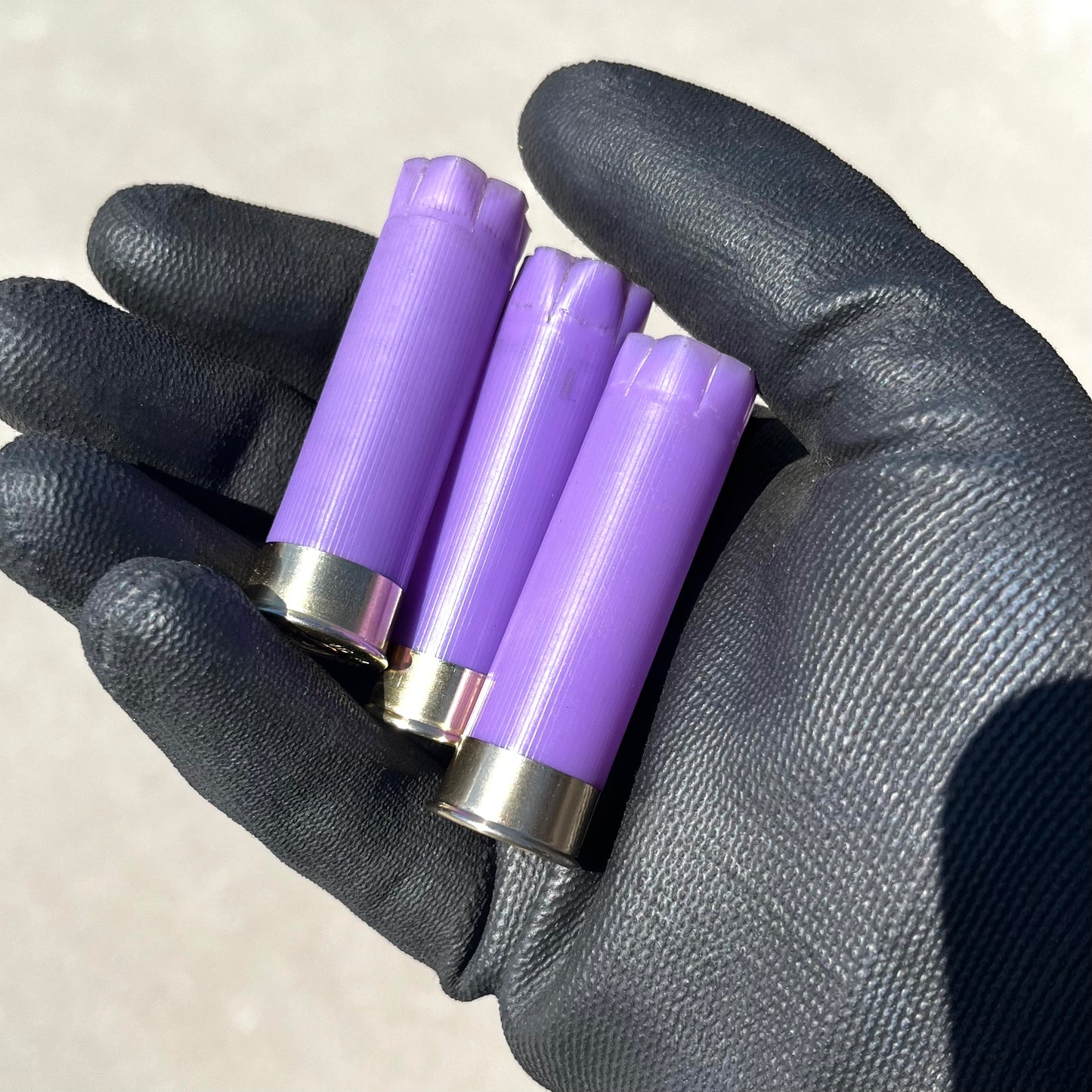 3 purple 16 gauge shotgun shell hulls held in a gloved hand
