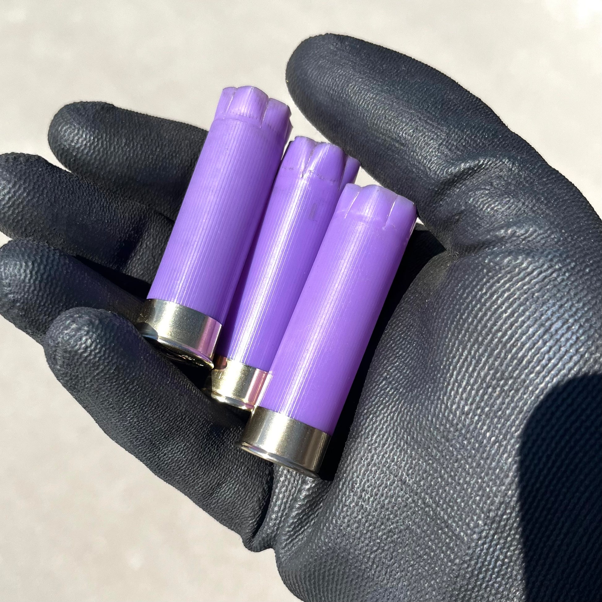3 purple 16 gauge shotgun shell hulls held in a gloved hand