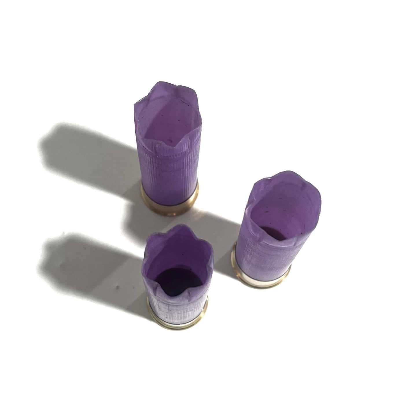 3 purple 16 gauge shotgun shell hulls with open crimped and cut ends, viewed from above