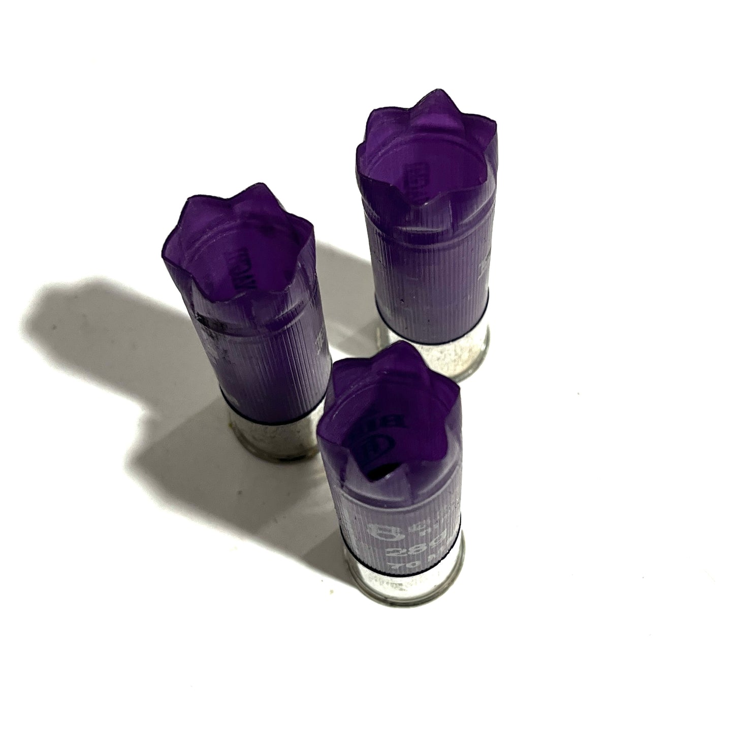 Three purple shotgun shells with silver high brass bottoms viewed from above showing fluted crimped tops