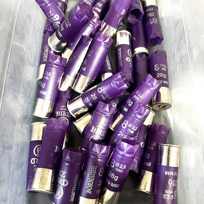 A large pile of purple Bornaghi shotgun shells with silver high brass bottoms in a plastic bin