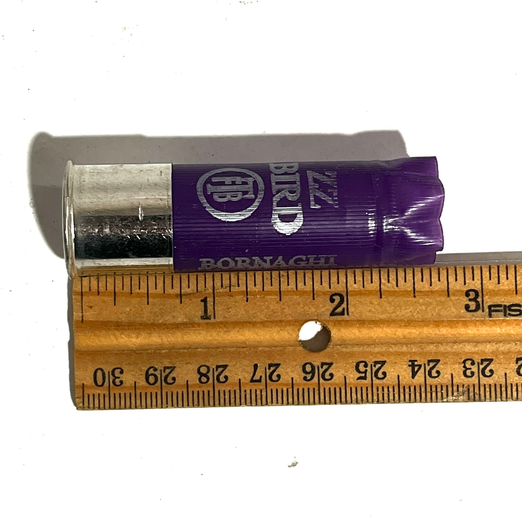 A purple Bornaghi shotgun shell with a silver high brass bottom beside a ruler showing a length of about 2.75 inches