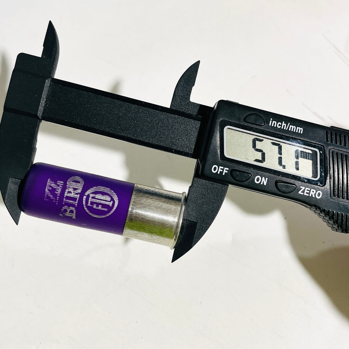 Digital caliper reading 57.1 mm along an empty purple casing, measured from the crimp end to the metal head