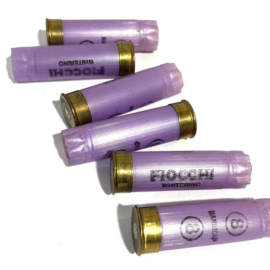 6 purple Fiocchi Whiterino 12 gauge shotgun shells with brass bases, lying on a white background