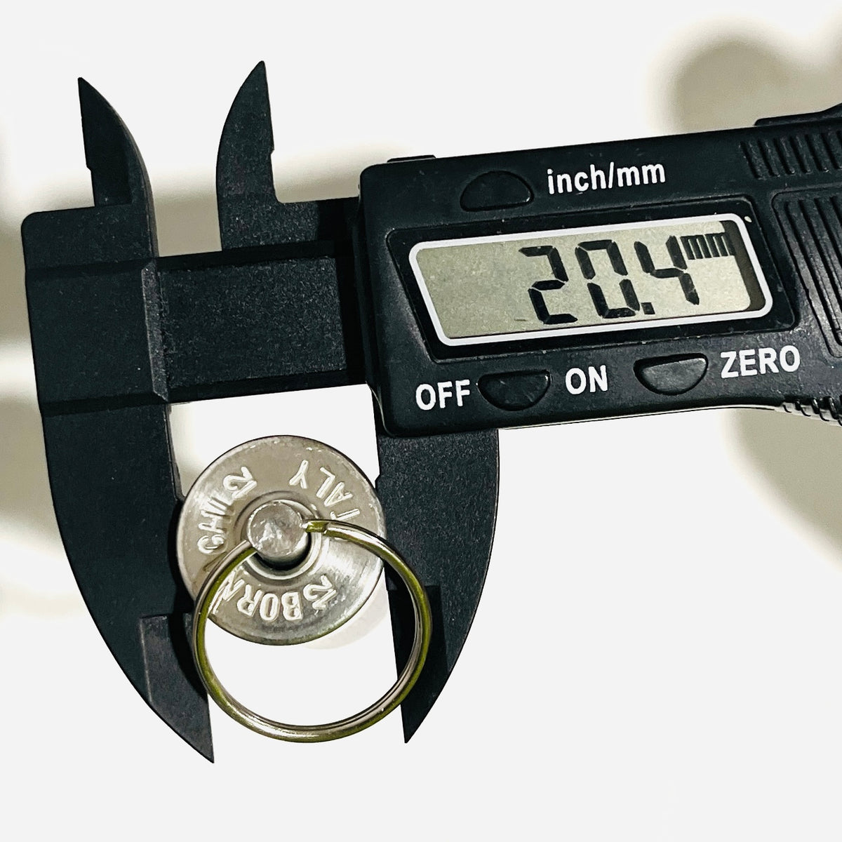 Digital caliper reading 20.4 mm across the rim of a once-fired hull keychain with split ring