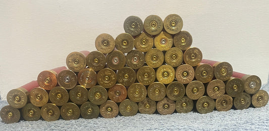 A large stack of gold and brass shotgun shell headstamps arranged in a pyramid with red hulls peeking out