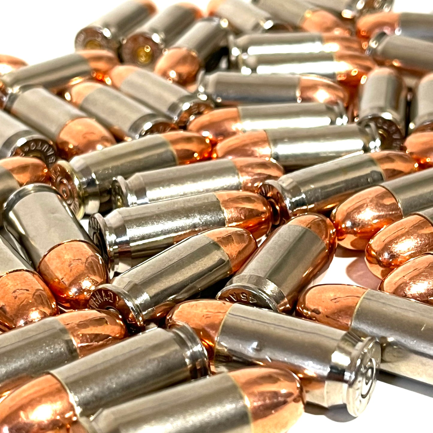 A large pile of nickel 45 ACP dummy rounds with copper round nose bullets scattered together for film props.