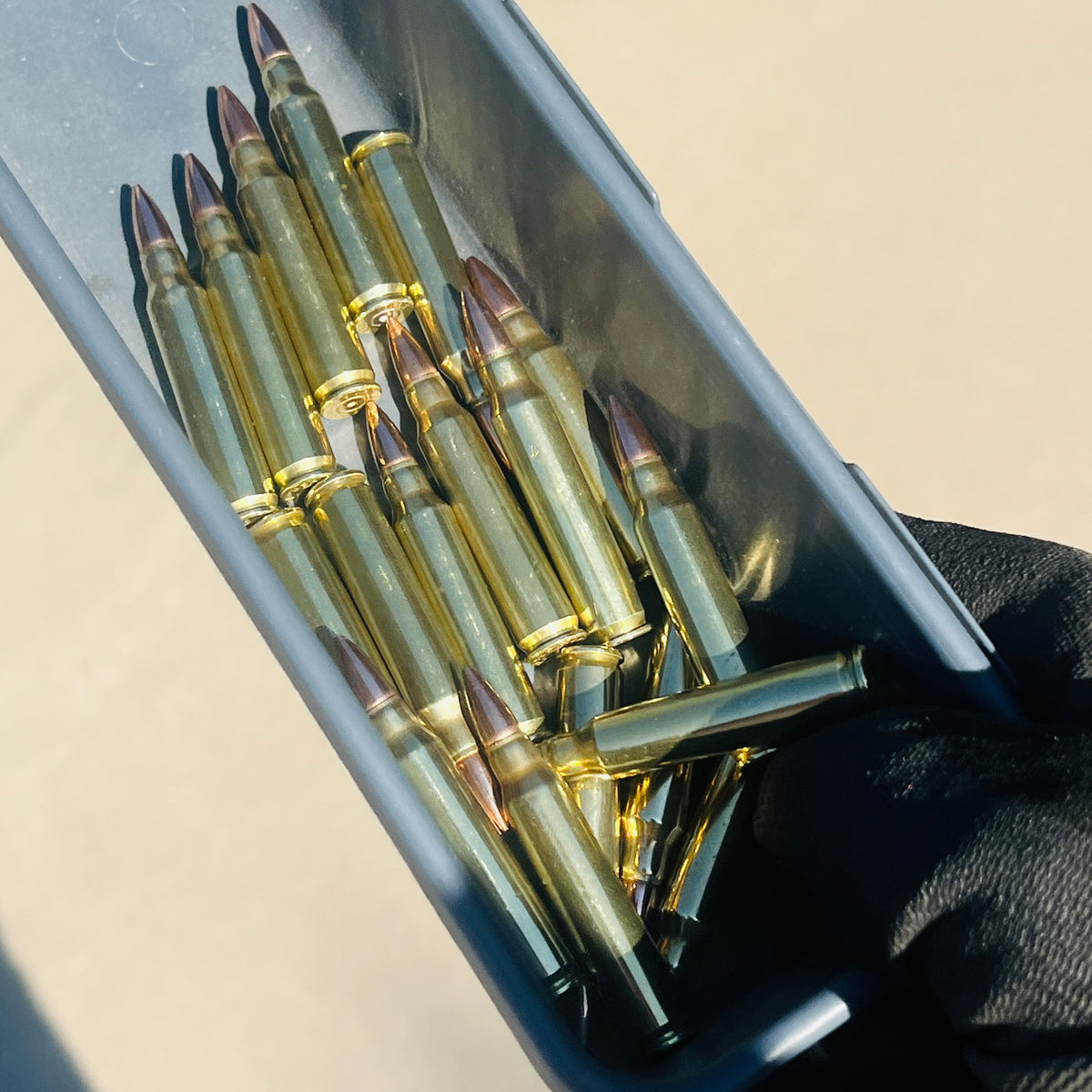 A gray container holding a bunch of 223 brass dummy rounds for fake ammunition for movie props in a black gloved hand