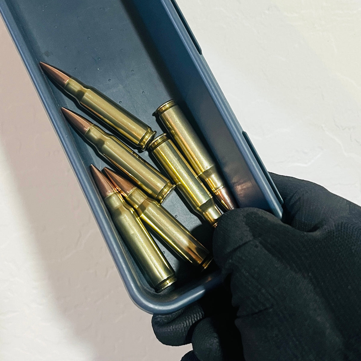 6 brass 308 realistic dummy rounds for props in a container held by black gloved hand
