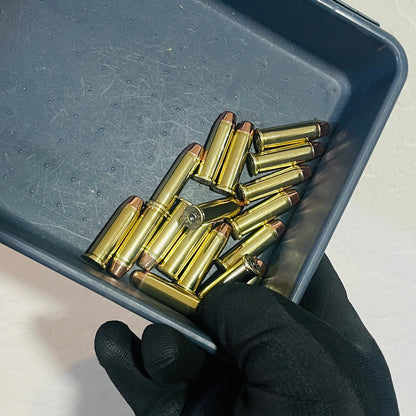 Pile of once-fired brass .38 Special fake ammunition dummy rounds with flat-nose bullets in a gray tray held by a black-gloved hand