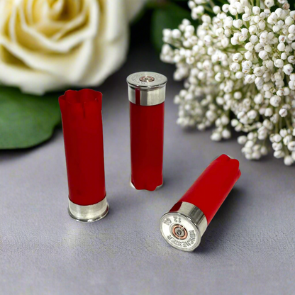 Three red shotgun shells with silver bottoms displayed among white rose and baby's breath flowers