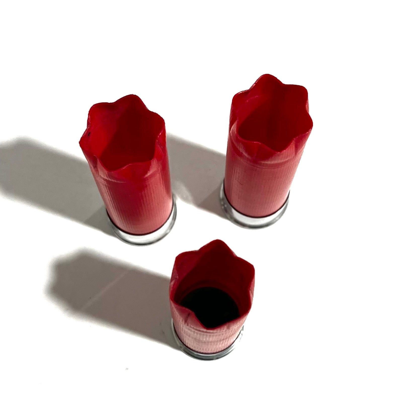 Three red shotgun shells with silver bottoms viewed from above showing fluted crimped tops