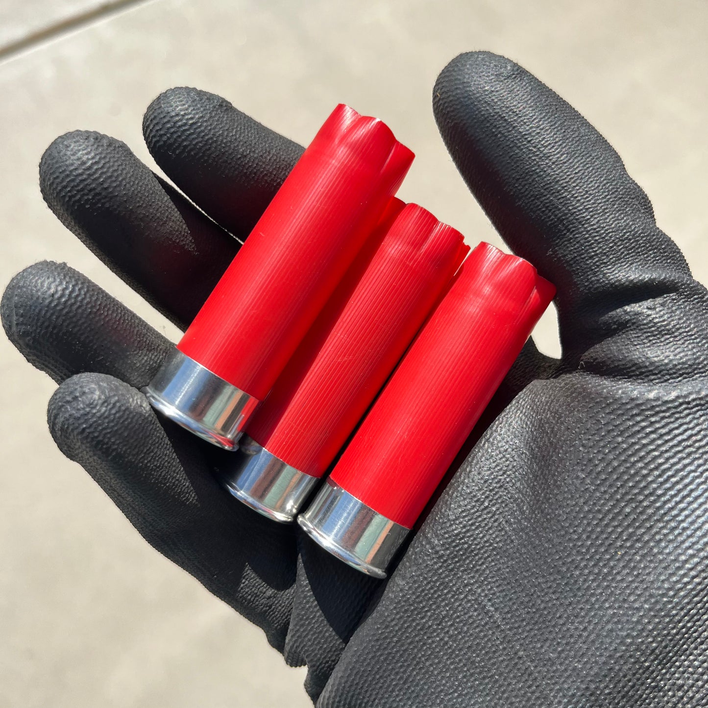 Three red shotgun shells with silver bottoms held in a black gloved hand