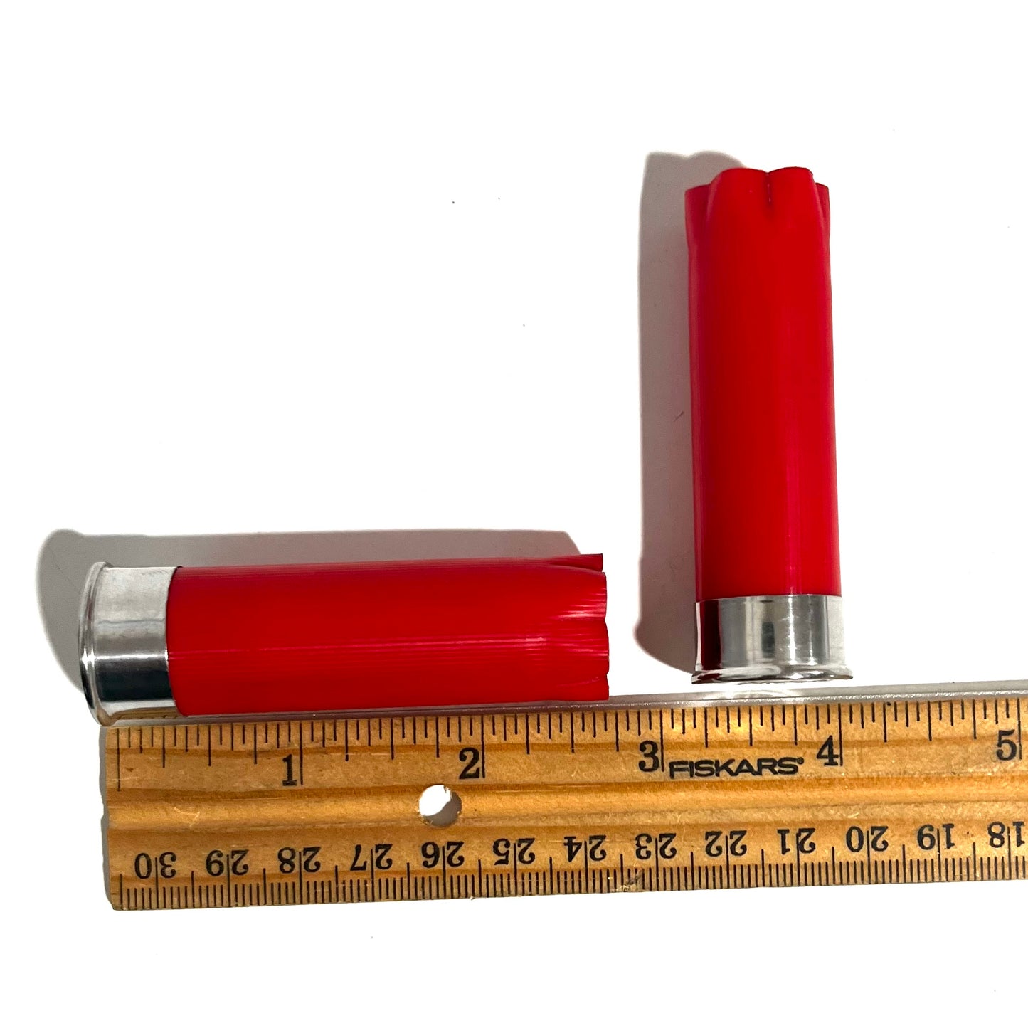 Two red shotgun shells with silver bottoms beside a ruler showing a length of about 2.75 inches