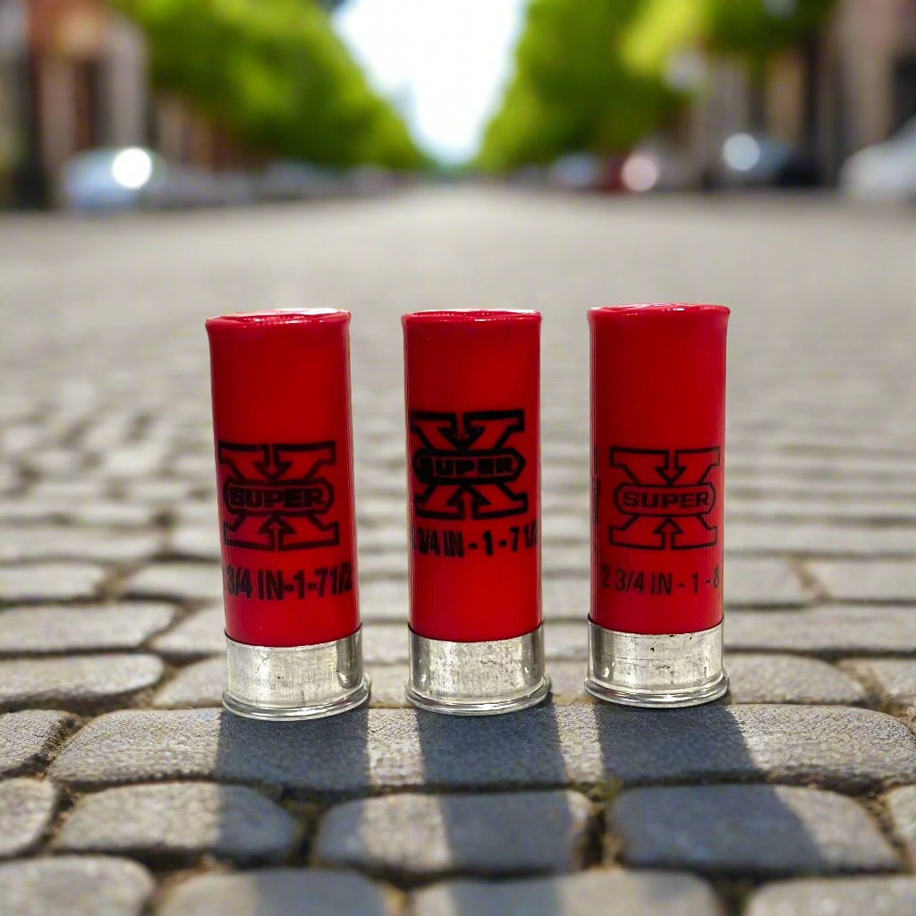 Three red once-fired hulls standing on cobblestone pavement with a blurred tree-lined street behind