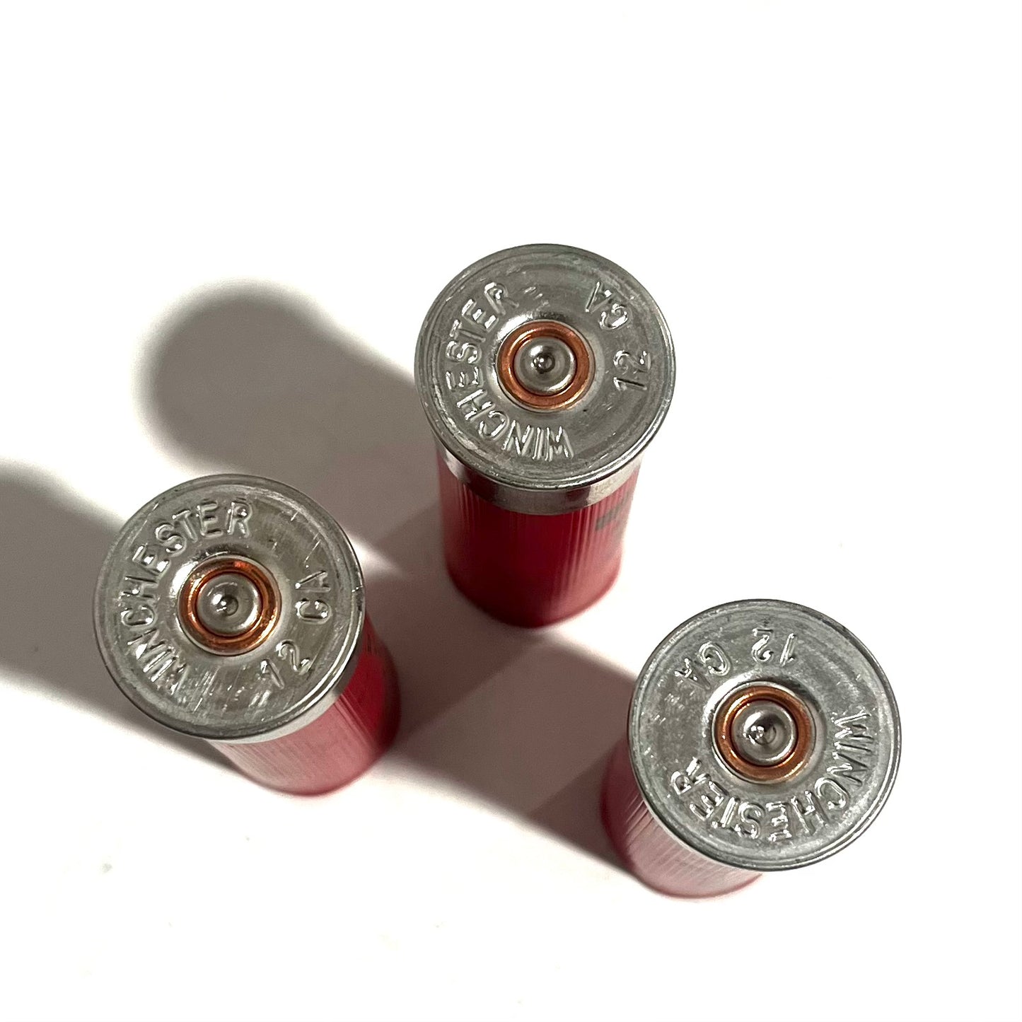 Three red spent dummy rounds shown base-up with legible headstamps and spent primers