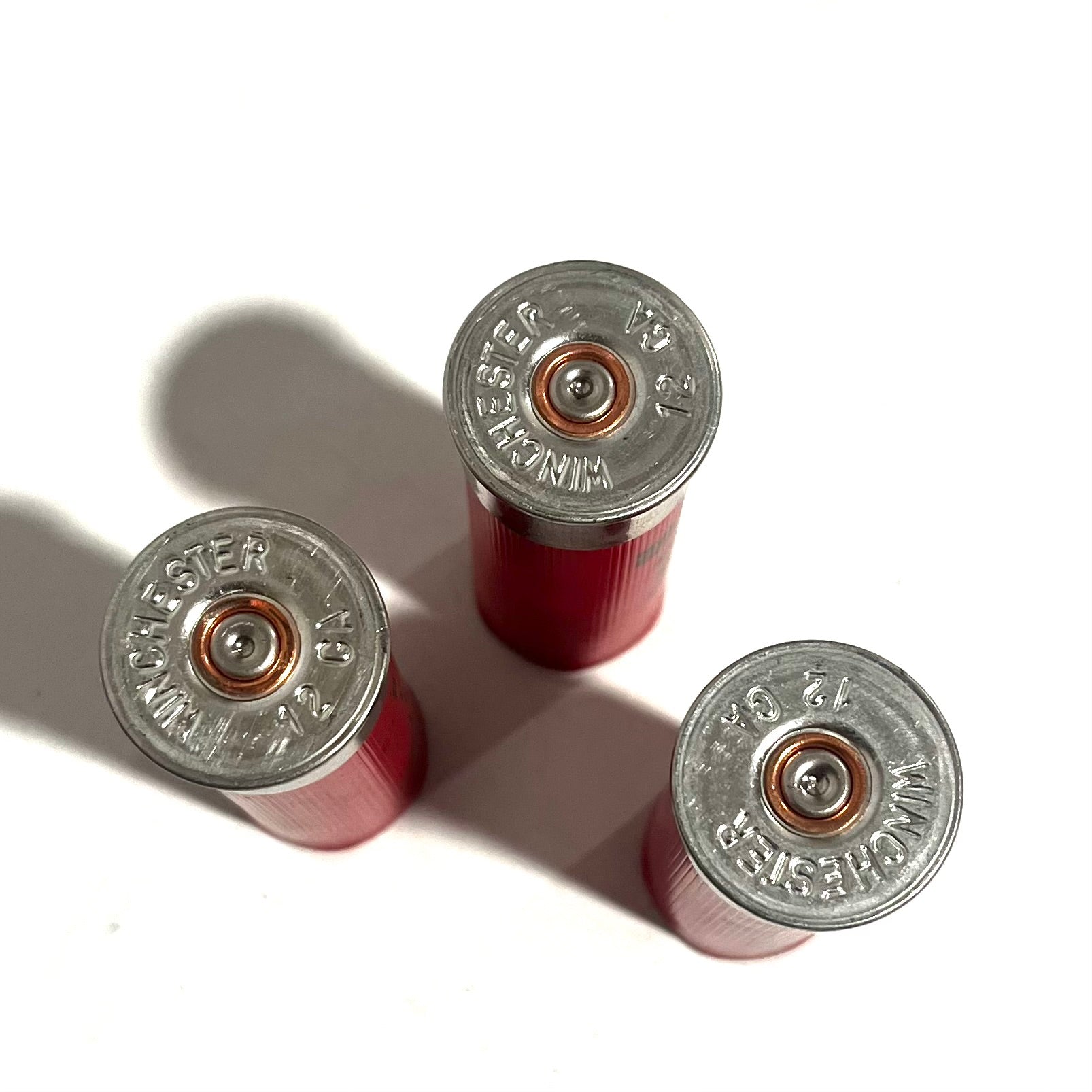 Three red spent dummy rounds shown base-up with legible headstamps and spent primers