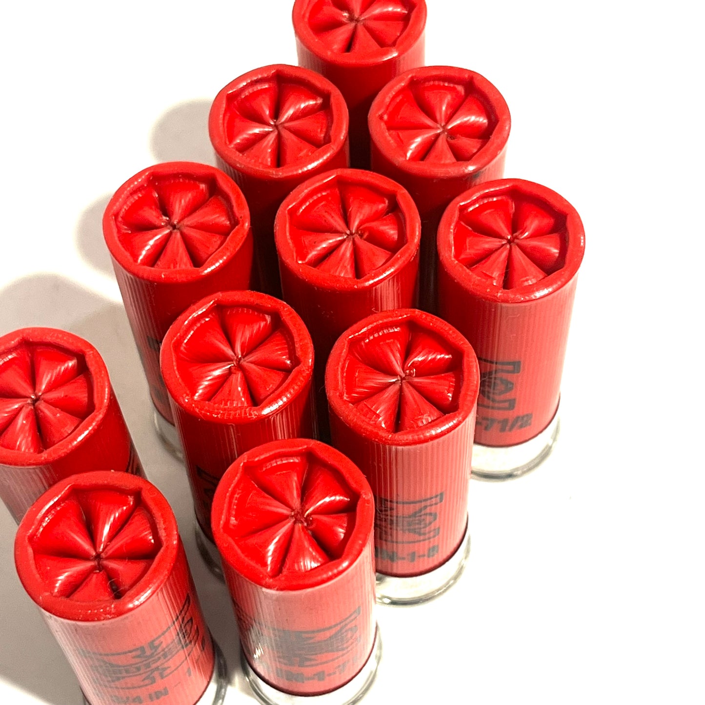 Ten red used casings clustered together at an angle showing star-crimped tops and worn sides