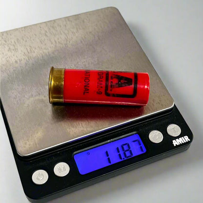 Single red Winchester AA International 12 gauge shotgun dummy round on a digital gram scale reading 11.87 grams