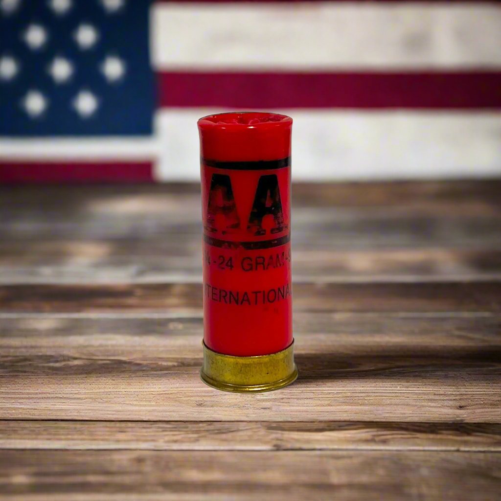 Single red Winchester AA International 12 gauge shotgun dummy round standing on wood plank in front of blurred American flag