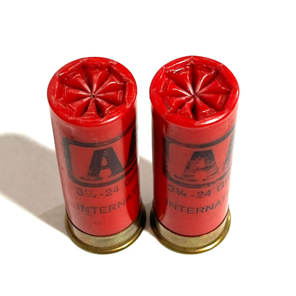 Two red Winchester AA International 12 gauge shotgun dummy rounds standing upright with star crimp tops, gold brass bases