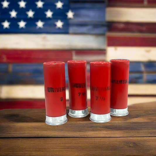Four red 12 gauge Winchester dummy rounds with silver bases standing on a wooden surface in front of an American flag.