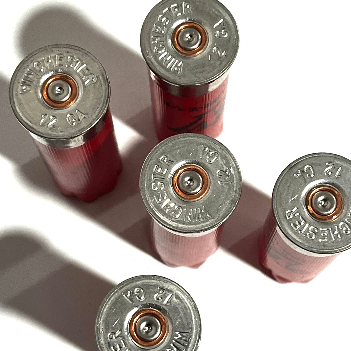 Five red Winchester 12 gauge empty shotgun shells with silver bases viewed from above on a white background