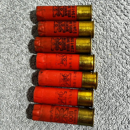 Seven red Winchester Super X 12 gauge empty shotgun shells with gold high brass bases lying on a gray carpet