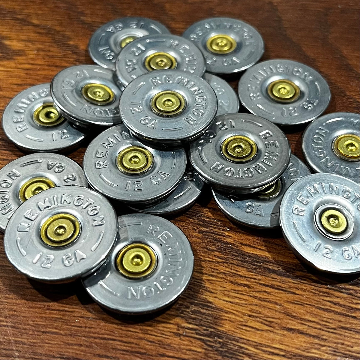 Pile of about 15 Remington 12 gauge shotgun shell slices on a wood surface, all showing the embossed headstamp face and brass primers