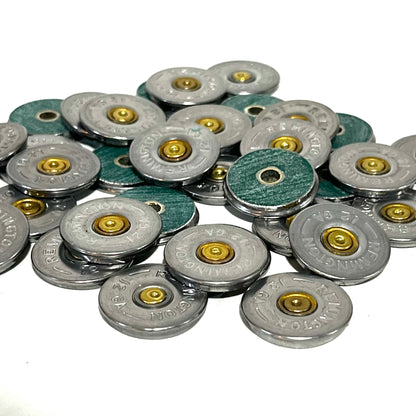 Large pile of Remington 12 gauge shotgun shell slices scattered on white background, showing a mix of silver headstamp faces and green hull-side faces with drilled center holes