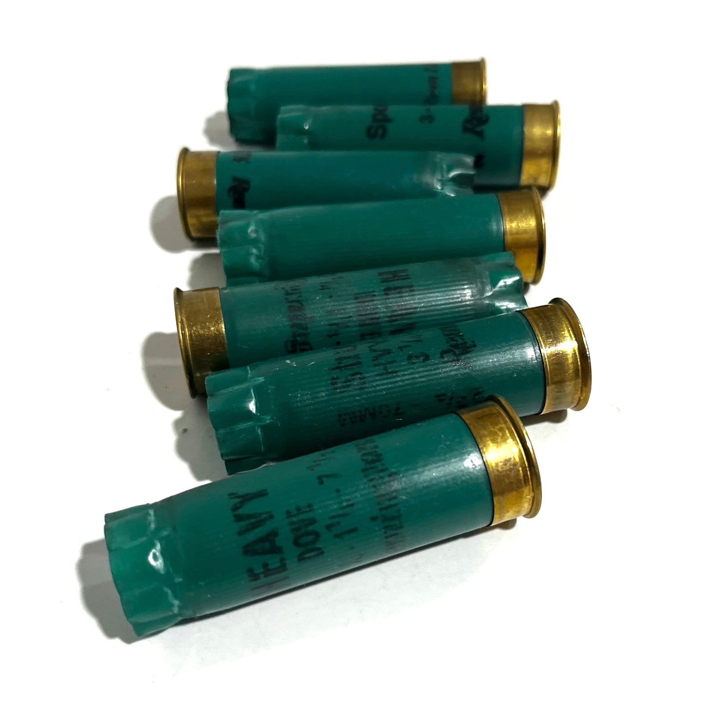 Seven dark green Remington 12 gauge empty shotgun shells with gold bases lying on a white background