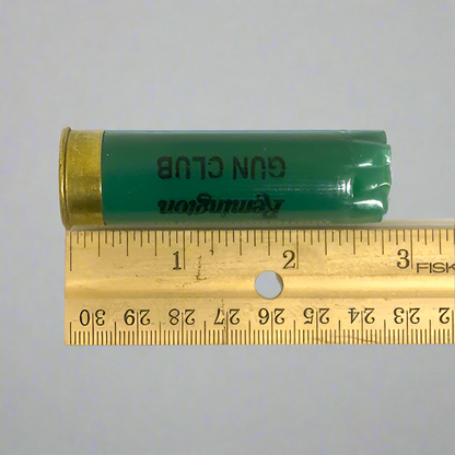 Green Remington Gun Club 12 gauge empty shotgun shell laid next to a wooden ruler showing a length of about 2.75 inches