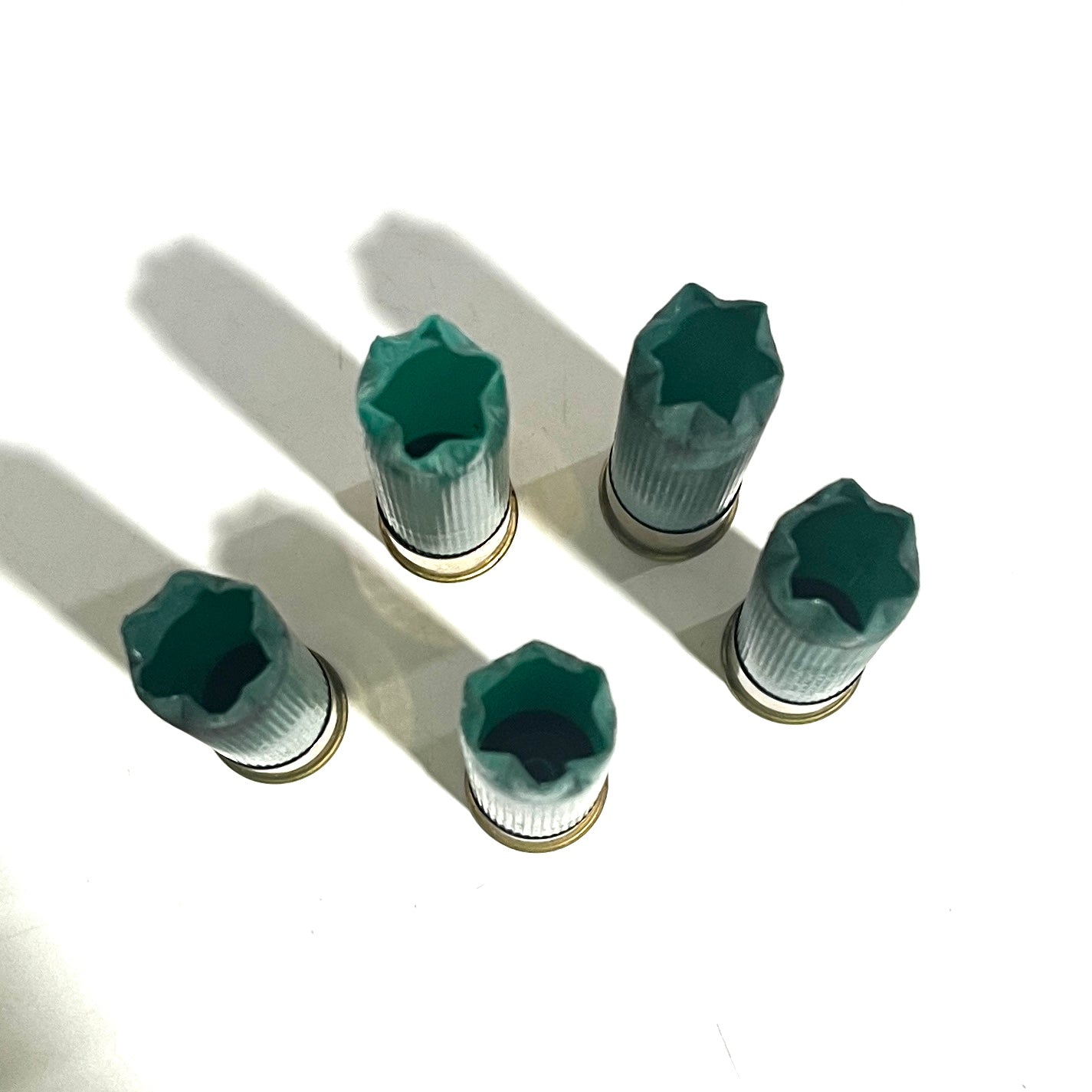 Top-down view of five green empty 28 gauge shotgun shells with open top 6 star crimps on a white surface.