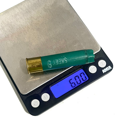 A green 28 gauge empty shotgun shell resting on a digital scale displaying a weight of 6.00 grams.