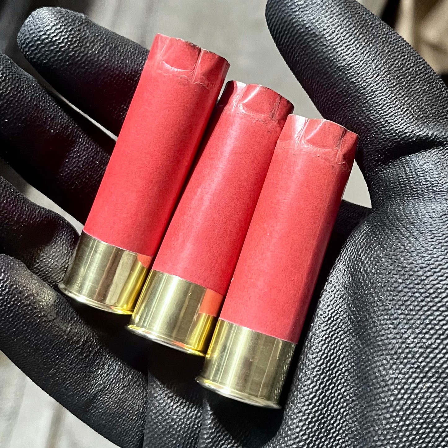 3 salmon pink paper shotgun shells with gold brass heads held in a black gloved hand
