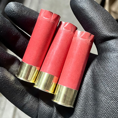 3 salmon pink paper shotgun shells with gold brass heads held in a black gloved hand