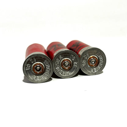 Three red dummy hulls lying flat with their silver metal bases showing Winchester 12 GA stamps.
