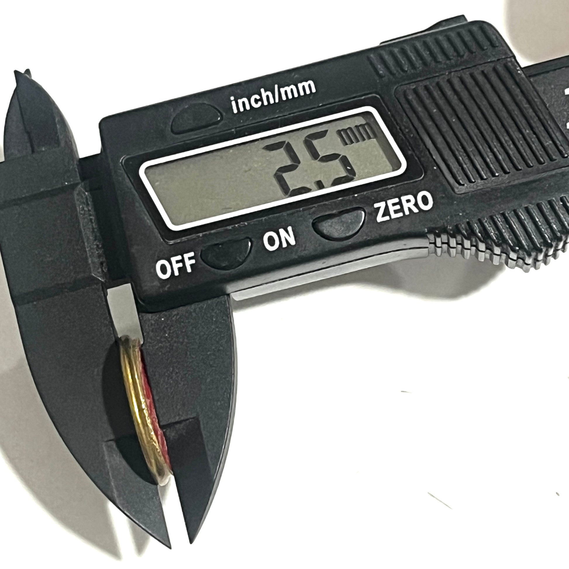 A digital caliper grips a gold shell shell deprimed slice on edge, showing a thickness reading of 2.5 mm.