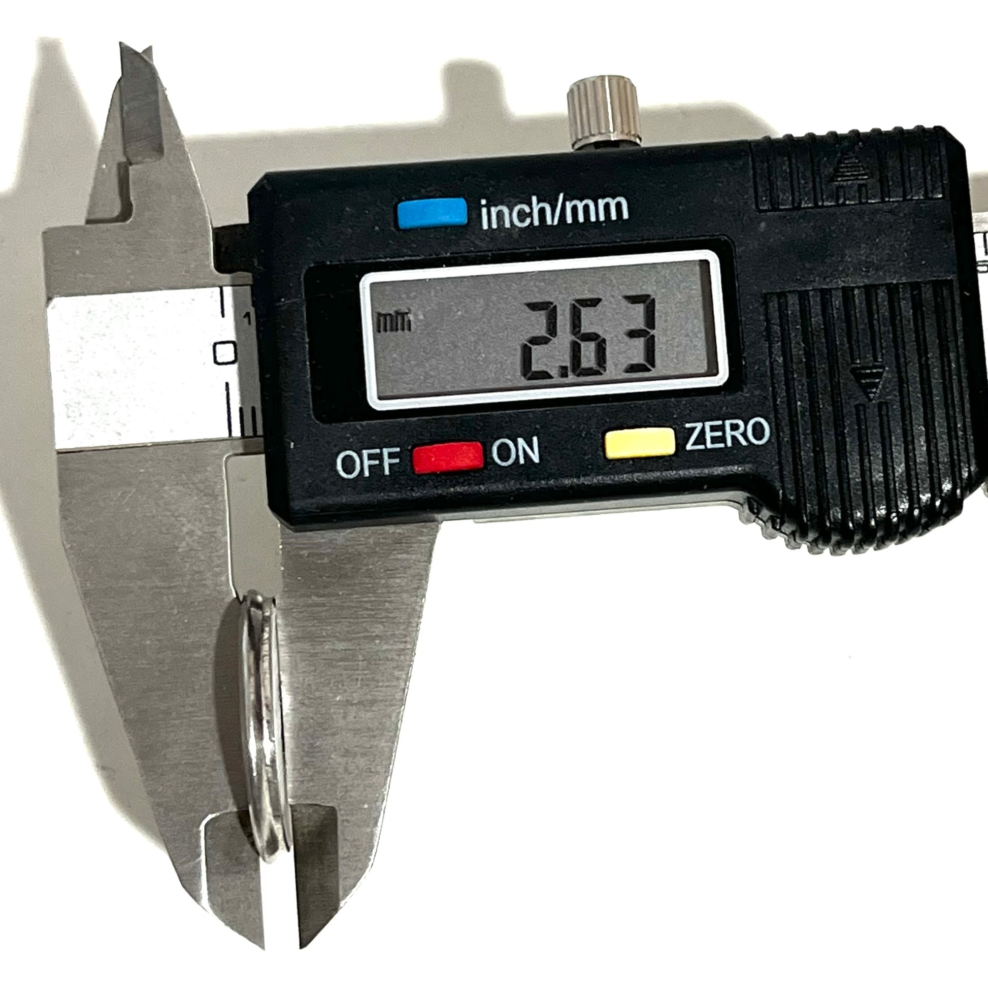 Digital caliper measuring the thickness of a silver shotgun shell slice showing 2.63 mm
