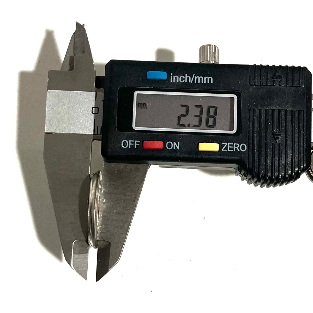 Digital caliper measuring the thickness of a silver shotgun shell slice at 2.38 mm