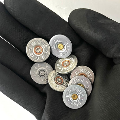 A handful of silver shotgun shell slices with various headstamps held in a black-gloved hand