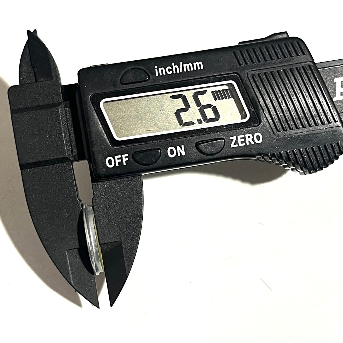 Winchester 20-gauge shotgun slice held edge-on in calipers showing 2.6 mm thickness for height