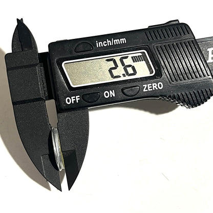 Winchester 20-gauge shotgun slice held edge-on in calipers showing 2.6 mm thickness for height